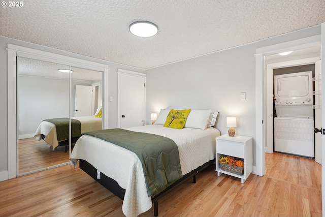 bedroom with stacked washing machine and dryer, light wood finished floors, a closet, a textured ceiling, and baseboards