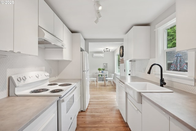 kitchen featuring white appliances, under cabinet range hood, a sink, light wood-style floors, and tasteful backsplash