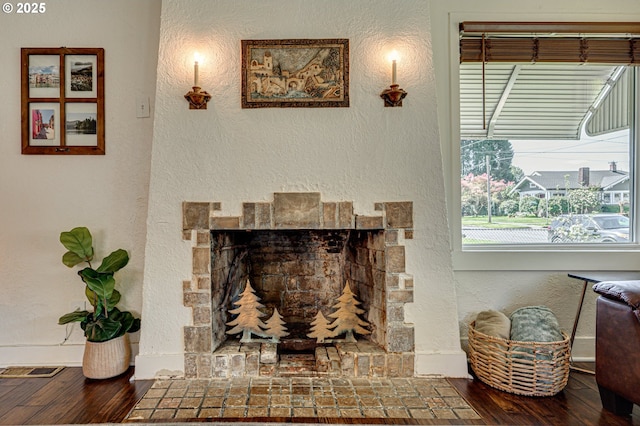 interior details featuring baseboards, a textured wall, wood finished floors, and a stone fireplace