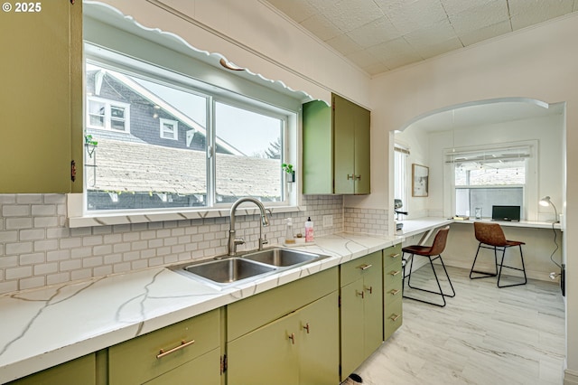 kitchen with ornamental molding, green cabinetry, arched walkways, a sink, and backsplash