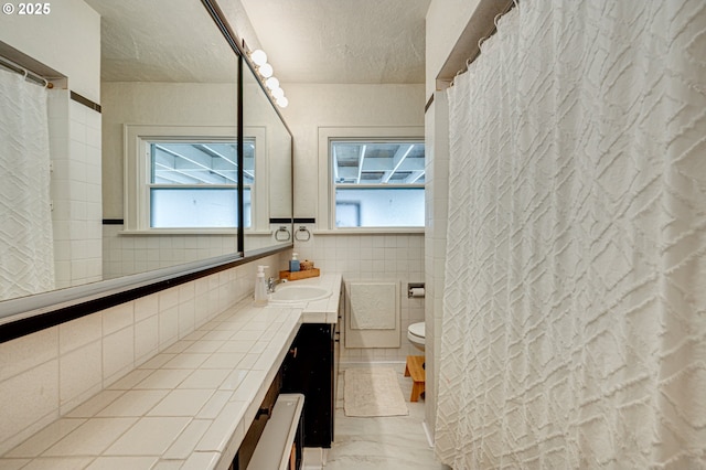 full bath featuring tile walls, vanity, toilet, and a textured ceiling
