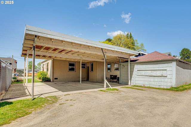 view of front of home with dirt driveway, fence, an attached carport, a shingled roof, and stucco siding