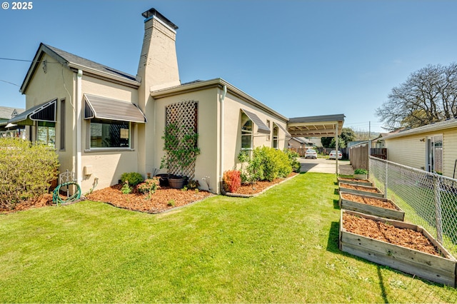 view of side of property featuring a garden, fence, stucco siding, a chimney, and a yard