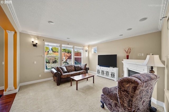 carpeted living area with baseboards, a textured ceiling, crown molding, ornate columns, and a fireplace