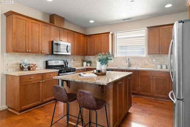 29229 SW Costa Cir E, Wilsonville, OR 97070 - kitchen with appliances with stainless steel finishes, a sink, light wood-style floors, a kitchen breakfast bar, and recessed lighting