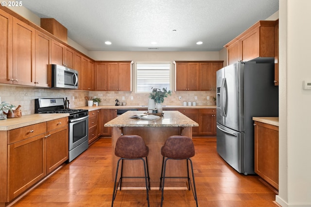 29229 SW Costa Cir E, Wilsonville, OR 97070 - kitchen with appliances with stainless steel finishes, a kitchen island, a breakfast bar area, light wood-type flooring, and recessed lighting