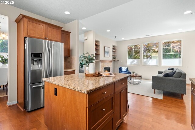 29229 SW Costa Cir E, Wilsonville, OR 97070 - kitchen with stainless steel fridge with ice dispenser, open floor plan, light wood-type flooring, light stone counters, and a center island