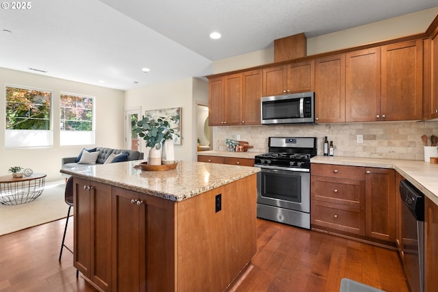 29229 SW Costa Cir E, Wilsonville, OR 97070 - kitchen with stainless steel appliances, dark wood finished floors, a center island, brown cabinetry, and recessed lighting