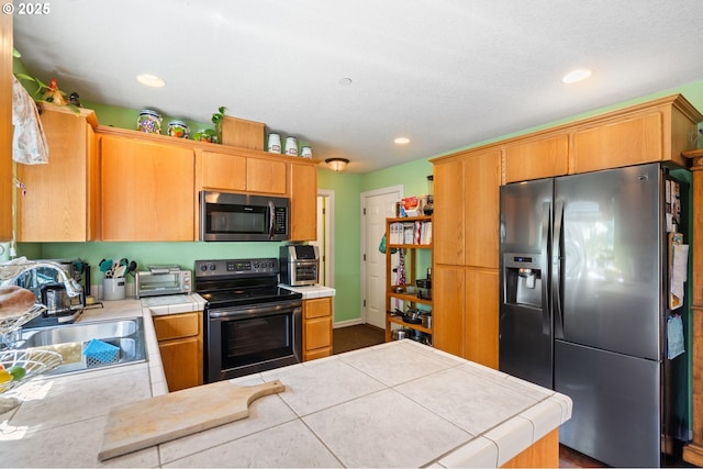 kitchen featuring stainless steel appliances, tile countertops, a sink, a peninsula, and recessed lighting