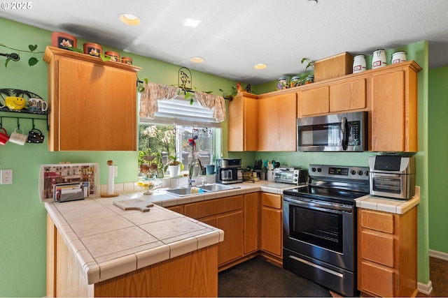 kitchen with appliances with stainless steel finishes, a sink, tile counters, and recessed lighting