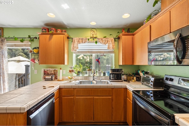 kitchen with appliances with stainless steel finishes, a sink, recessed lighting, a peninsula, and tile countertops