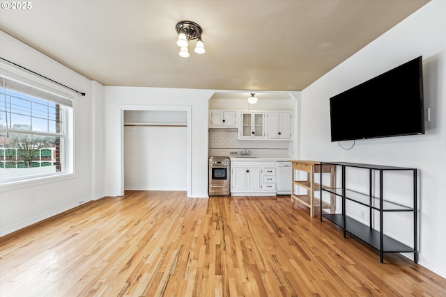 unfurnished living room with light wood-type flooring, a sink, and baseboards