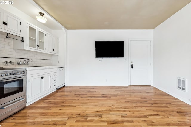 kitchen with stainless steel range, light wood-type flooring, visible vents, and decorative backsplash