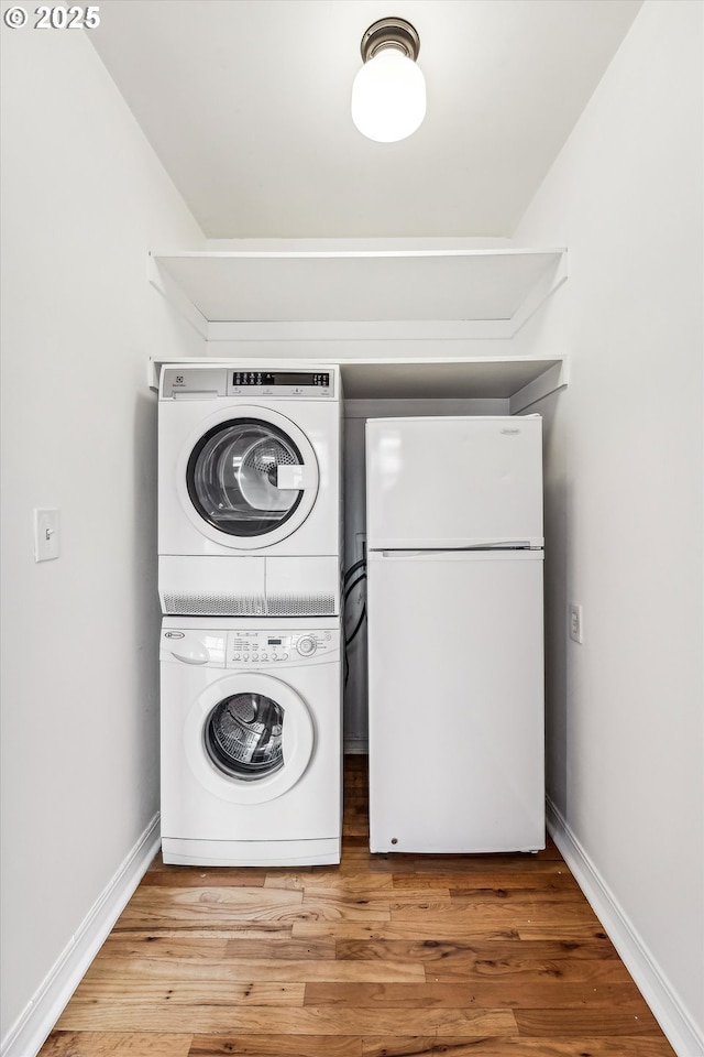 washroom featuring light wood-type flooring, stacked washer / drying machine, laundry area, and baseboards