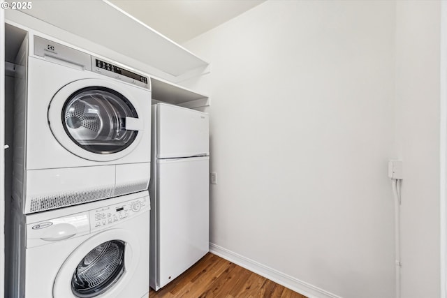 washroom featuring stacked washer / drying machine, laundry area, baseboards, and wood finished floors