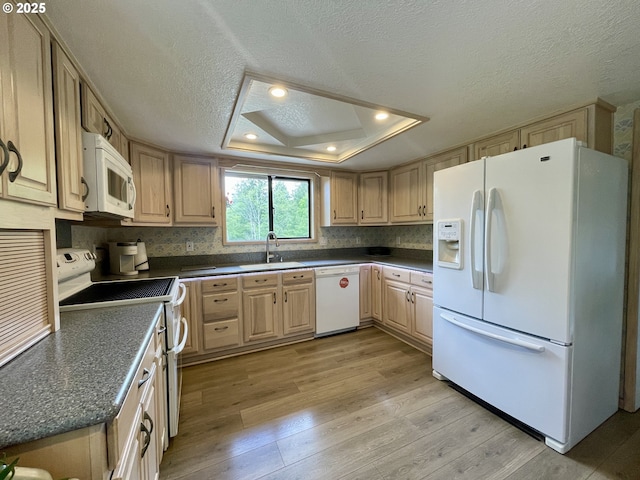 kitchen featuring white appliances, dark countertops, light wood finished floors, a sink, and a textured ceiling