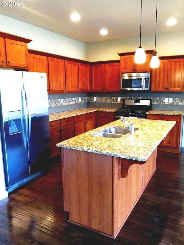 kitchen featuring a kitchen island with sink, dark wood finished floors, decorative light fixtures, appliances with stainless steel finishes, and decorative backsplash