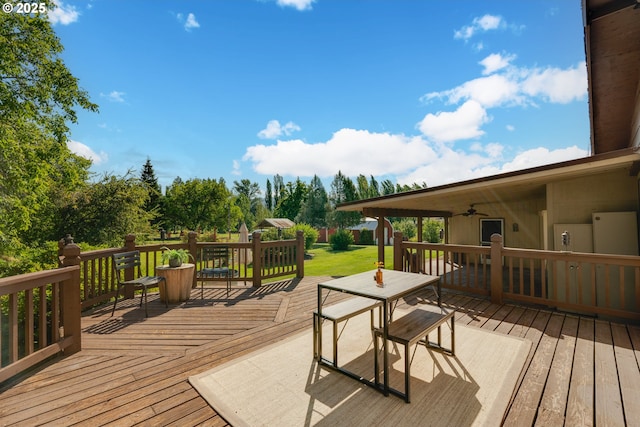 wooden deck with outdoor dining area, a ceiling fan, and a yard