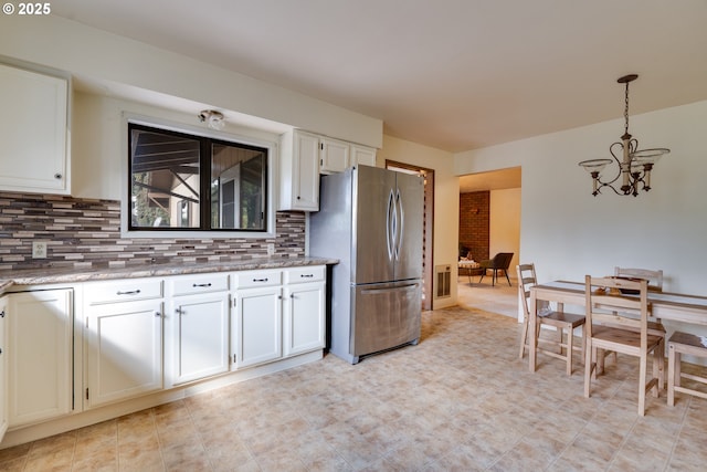 kitchen featuring decorative light fixtures, tasteful backsplash, an inviting chandelier, freestanding refrigerator, and white cabinets