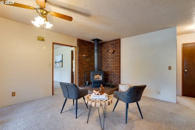 sitting room featuring a wood stove, ceiling fan, a textured ceiling, and light colored carpet