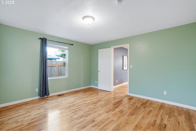 unfurnished room featuring light wood-type flooring, a textured ceiling, baseboards, and visible vents