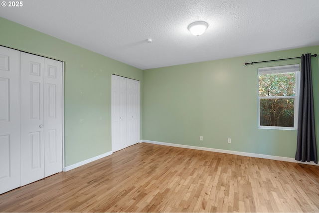 unfurnished bedroom featuring baseboards, two closets, light wood-type flooring, and a textured ceiling