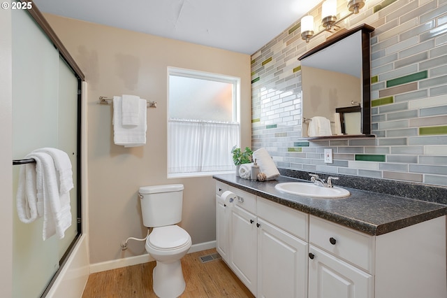 bathroom featuring a shower with shower door, wood finished floors, baseboards, vanity, and toilet