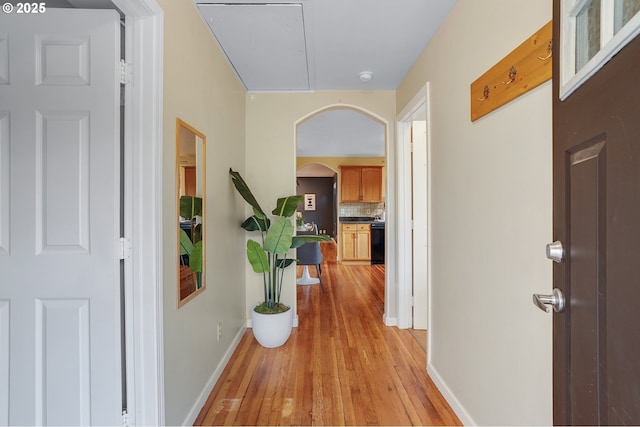 corridor with baseboards, arched walkways, and light wood finished floors