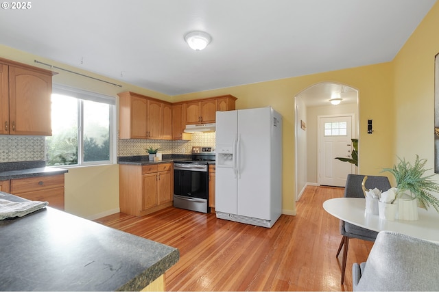 kitchen featuring arched walkways, light wood-type flooring, stainless steel range with electric stovetop, white fridge with ice dispenser, and under cabinet range hood