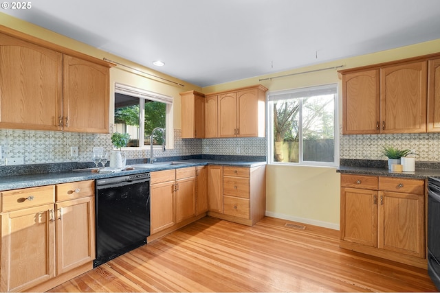 kitchen with visible vents, black dishwasher, tasteful backsplash, a sink, and light wood finished floors