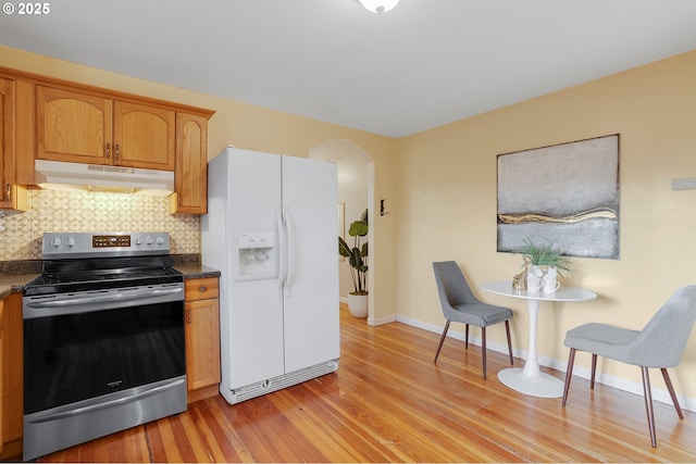 kitchen featuring white refrigerator with ice dispenser, light wood finished floors, arched walkways, under cabinet range hood, and stainless steel electric stove