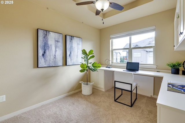 home office featuring a raised ceiling, light colored carpet, a ceiling fan, built in study area, and baseboards