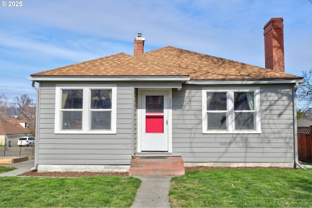 bungalow with a front yard, fence, a shingled roof, entry steps, and a chimney