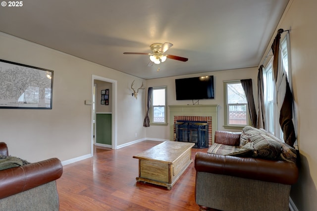 living area with a wealth of natural light, a brick fireplace, baseboards, and wood finished floors