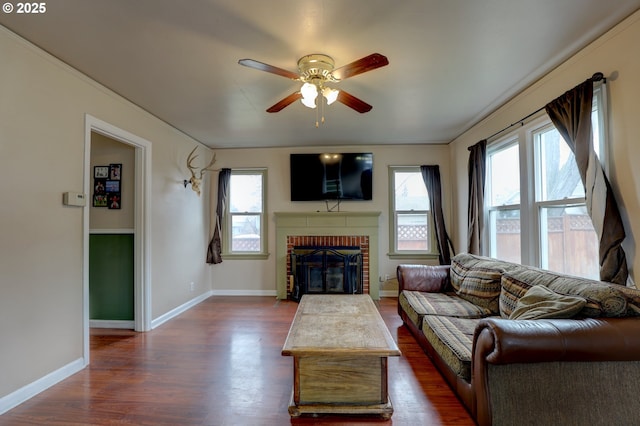 living room with dark wood-type flooring, a brick fireplace, baseboards, and ceiling fan