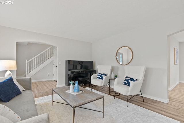 living room with light wood-style flooring, stairs, baseboards, and arched walkways