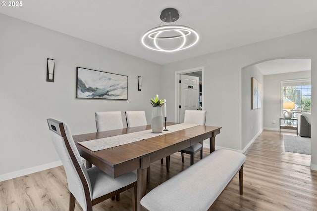 dining room with light wood-type flooring, arched walkways, and baseboards