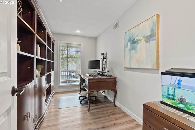 office area featuring light wood-style flooring, a textured ceiling, visible vents, and baseboards