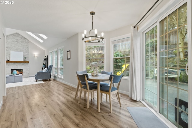 dining area featuring light wood-type flooring, a wealth of natural light, vaulted ceiling, and a stone fireplace