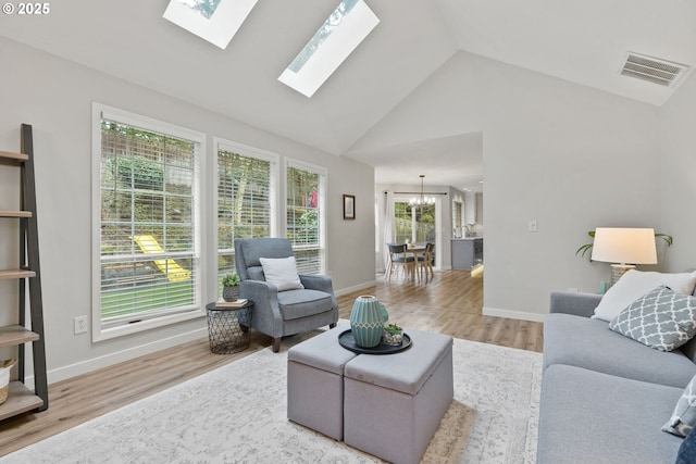 living area with a skylight, visible vents, an inviting chandelier, high vaulted ceiling, and light wood-type flooring