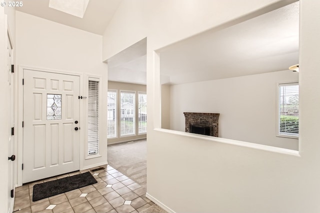 entrance foyer featuring a fireplace, light tile patterned floors, lofted ceiling, light carpet, and baseboards