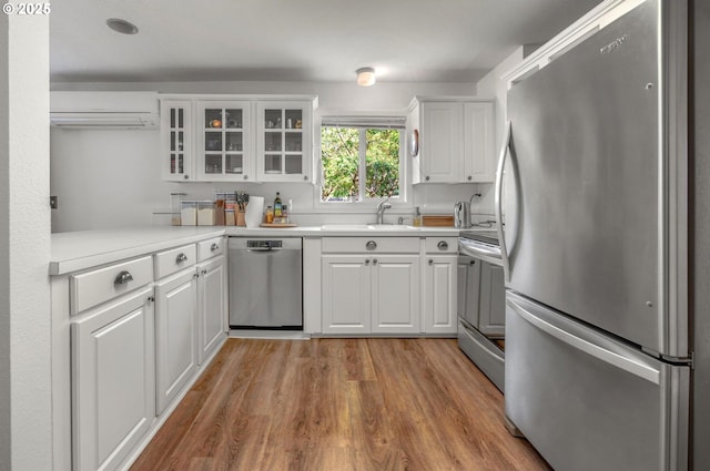 11144 NE Knott St, Portland, OR 97220 - kitchen with stainless steel appliances, a wall mounted air conditioner, glass insert cabinets, white cabinetry, and light wood-type flooring