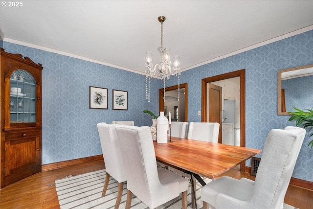 dining room with a notable chandelier, ornamental molding, and light wood-type flooring