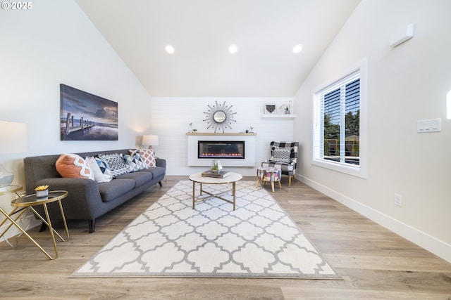 living room featuring high vaulted ceiling, recessed lighting, baseboards, light wood finished floors, and a glass covered fireplace