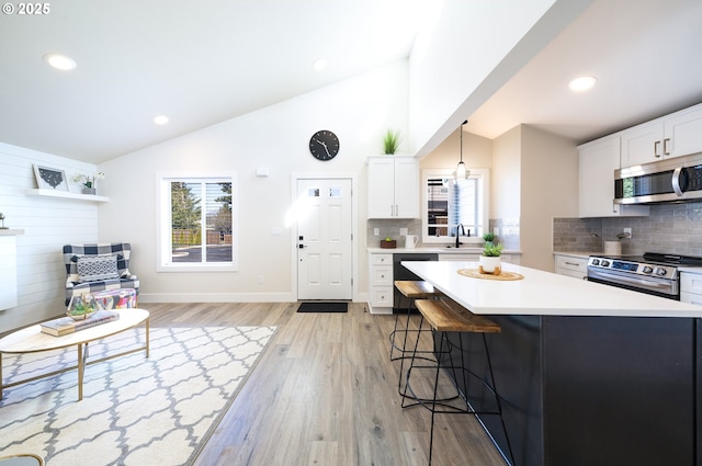 kitchen featuring a center island, stainless steel appliances, light countertops, hanging light fixtures, and white cabinets