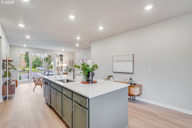 kitchen with a sink, an island with sink, gray cabinets, light wood-type flooring, and stainless steel dishwasher