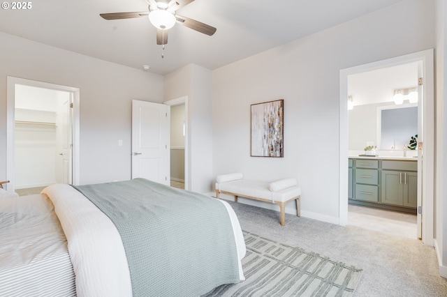 bedroom with a walk in closet, ceiling fan, light colored carpet, baseboards, and ensuite bath