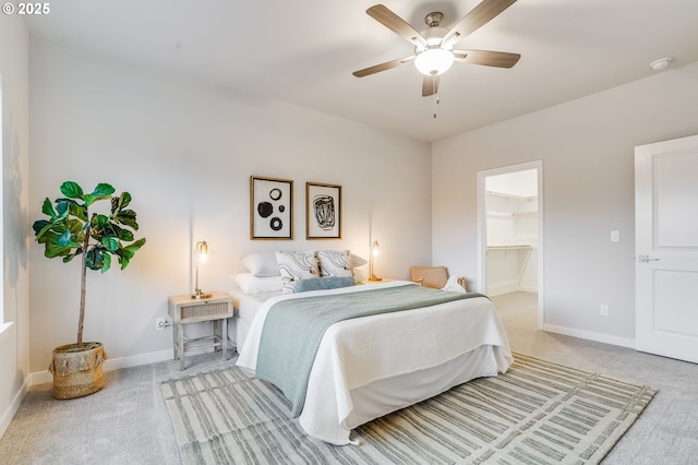 bedroom with baseboards, a ceiling fan, a spacious closet, and light carpet