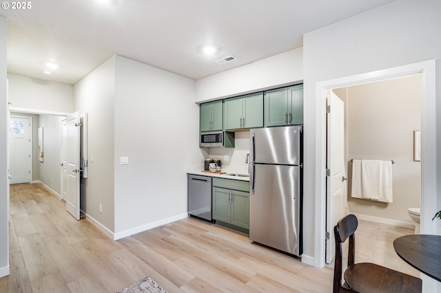 kitchen with green cabinetry, stainless steel appliances, light wood finished floors, and visible vents