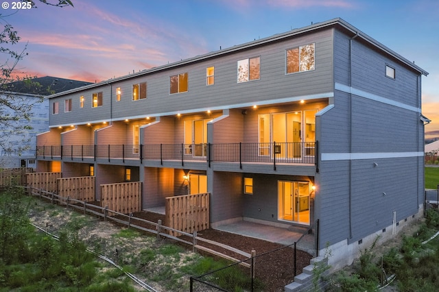 back of house at dusk with a patio, fence, and a balcony